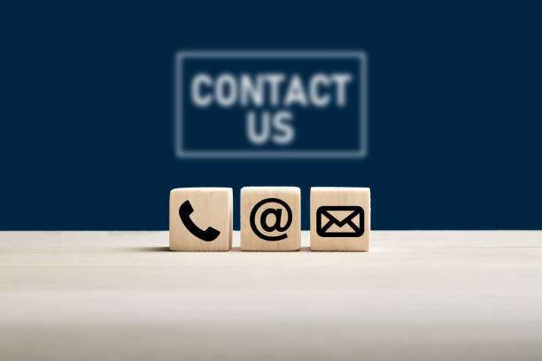 Phone and e-mail icons on wooden cubes with contact us text on blue background. Website page contact us or e-mail marketing concept.